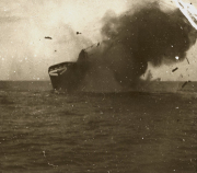 Ein Handelsschiff mit deutlicher Schlagseite und starker Rauchentwicklung sinkt auf hoher See. Die Aufnahme zeigt das Schiff kurz vor dem endgültigen Untergang während einer U-Boot-Versenkung im Ersten Weltkrieg.