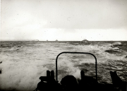 Aufnahme von der Brücke eines U-Bootes bei schwerem Seegang mit Blick auf mehrere Kriegsschiffe am Horizont. Im Vordergrund sind die Silhouetten von Turmaufbauten und Ausrüstung des fotografierenden U-Bootes zu erkennen.