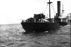 Ein Kriegsschiff mit einem Schornstein und sichtbaren Kampfschäden am Heck fährt durch bewegte See. Die Aufnahme zeigt deutliche Zerstörungen an der Heckpartie des Schiffes.