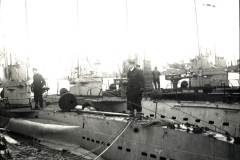 Mehrere deutsche U-Boote liegen nebeneinander in einem Hafen, wobei Besatzungsmitglieder auf den Decks und Türmen zu sehen sind. Die Aufnahme zeigt die charakteristischen Rümpfe und Aufbauten der Unterseeboote der Kaiserlichen Marine.