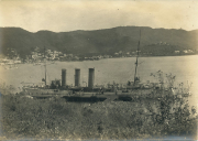 Kriegsschiff mit drei Schornsteinen im Hafen vor Gebirgslandschaft
