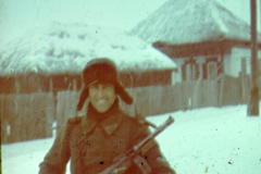 Soldat mit Gewehr vor russischen Holzbauten im Schnee