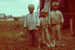 Drei Kinder in traditioneller russischer Kleidung vor Bauernhof