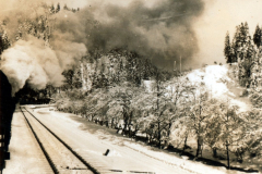 Eisenbahnstrecke in Berglandschaft mit Schnee und Rauchentwicklung