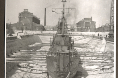 Kriegsschiff im Winterhafen mit Flakgeschütz und Industrieanlagen