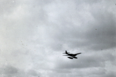 Militärflugzeug im Flug über Flugplatz mit Hangar