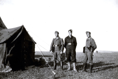 Drei Soldaten in Felduniform vor Feldlager in flacher Landschaft