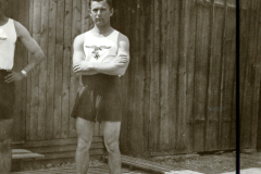 Mann in Sportkleidung mit NS-Symbolik vor Holzbaracke